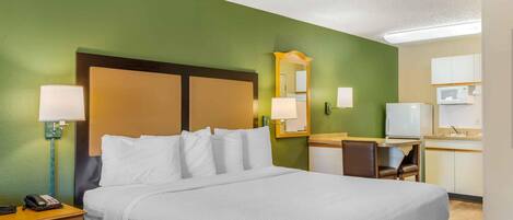 A hotel room with a large bed, bedside lamps, a desk with a chair, a television, and a microwave in the kitchenette.