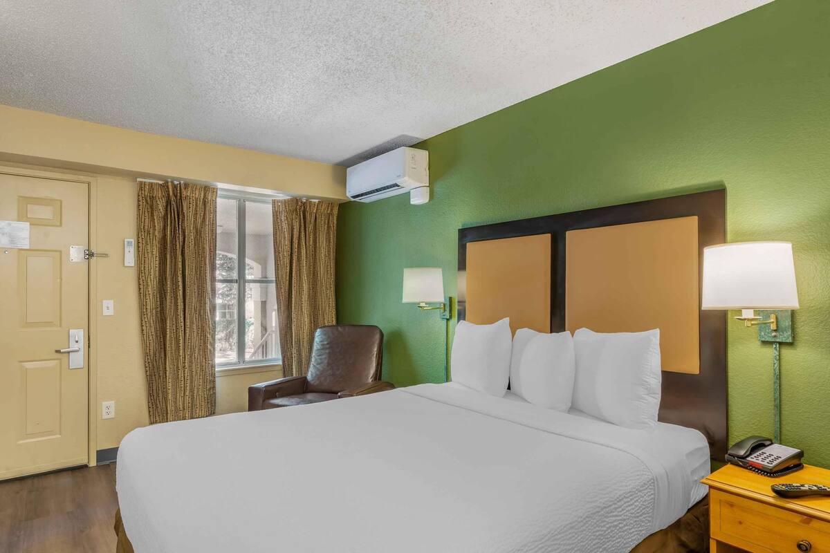 Une chambre d’hôtel avec un grand lit, une chaise, une table de chevet avec une lampe et un appareil de climatisation.