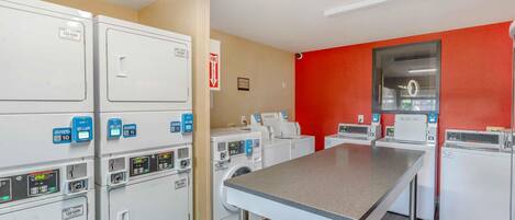 A laundry room with multiple washing machines and dryers, a table, and a fire exit sign.