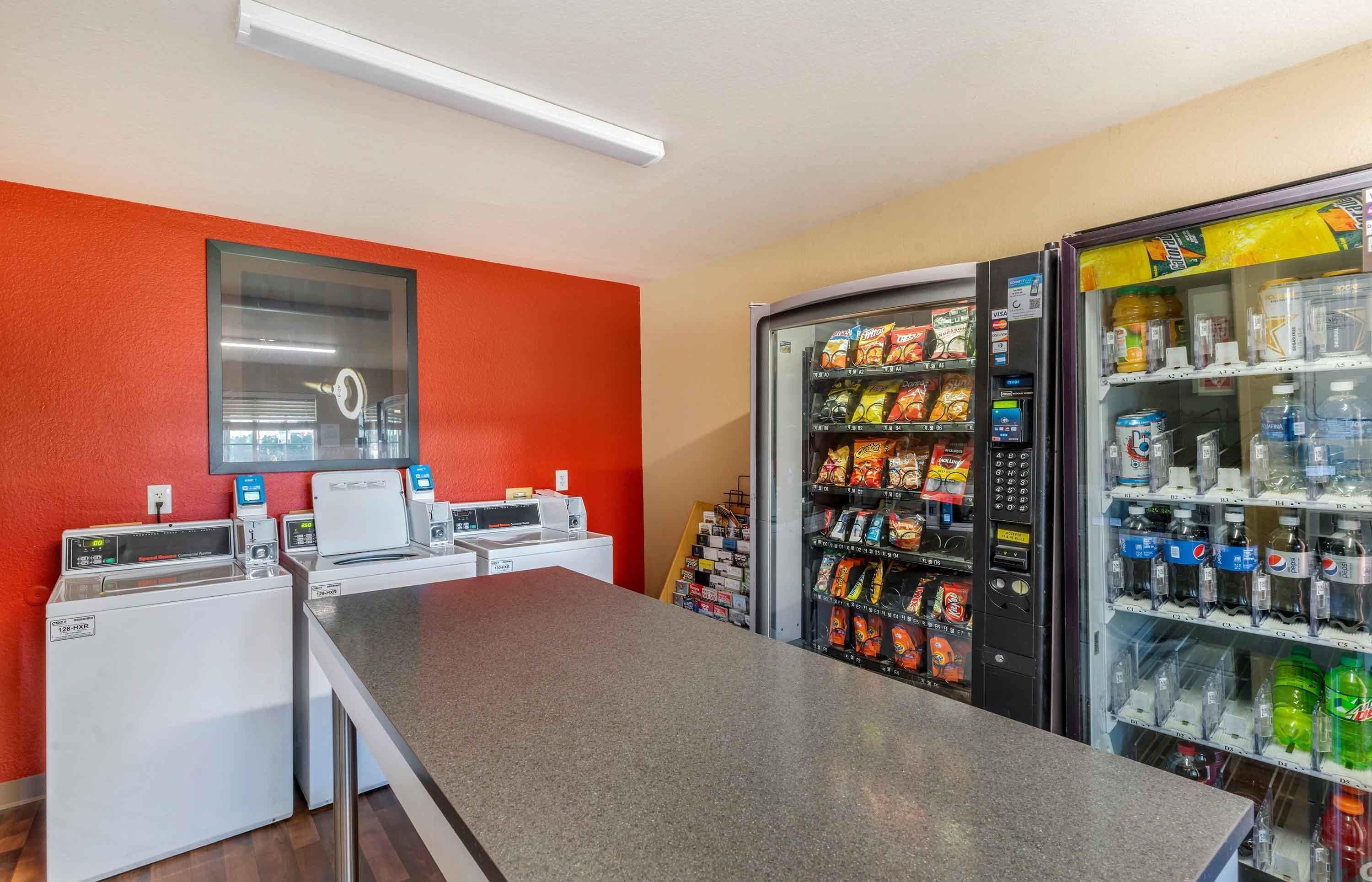 Ein Waschbereich mit Waschmaschinen, ein Getränkeautomaten für Snacks und ein Wasserspender.