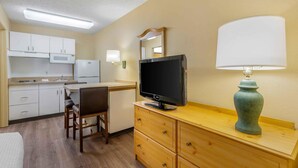 A compact hotel room with a kitchenette, a flat-screen TV, a wooden dresser, and a lamp. - Extended Stay America Suites Portland Beaverton (Beaverton)