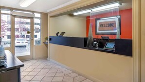 Et receptionsområde med et 'WELCOME'-skilt, en receptionsdisk, en computer og udsigt til parkeringspladsen.