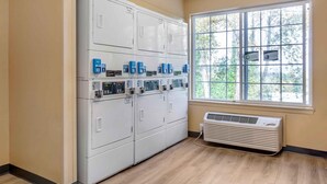 Et vaskerum med flere vaskemaskiner og tørretumblere, et vindue med udsigt til træer og en aircondition.