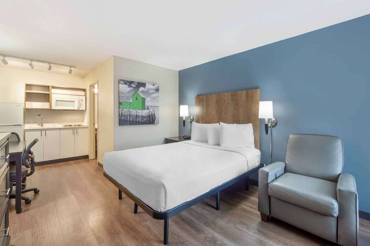 Una habitación de hotel con cama, una silla, un escritorio y una kitchenette.
