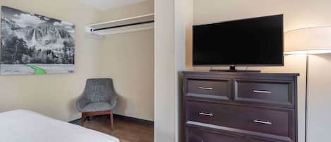 Habitación de hotel con cama, televisor de pantalla plana, cómoda, una silla y un cuadro de un paisaje montañoso.