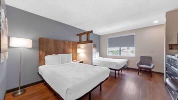 Une chambre d’hôtel avec deux lits, une tête de lit en bois, une lampe sur pied, une chaise et une commode.