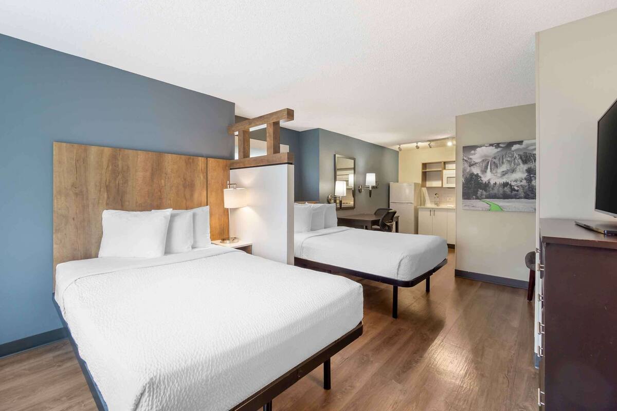 Una habitación de hotel con dos camas, un cabecero de madera, un escritorio y una silla.