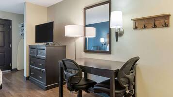 A hotel room with a desk, two office chairs, a television, a dresser, and a mirror.