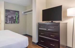 Habitación de hotel con cama, televisor sobre una cómoda, pintura de la Space Needle de Seattle y unidad de aire acondicionado de pared.