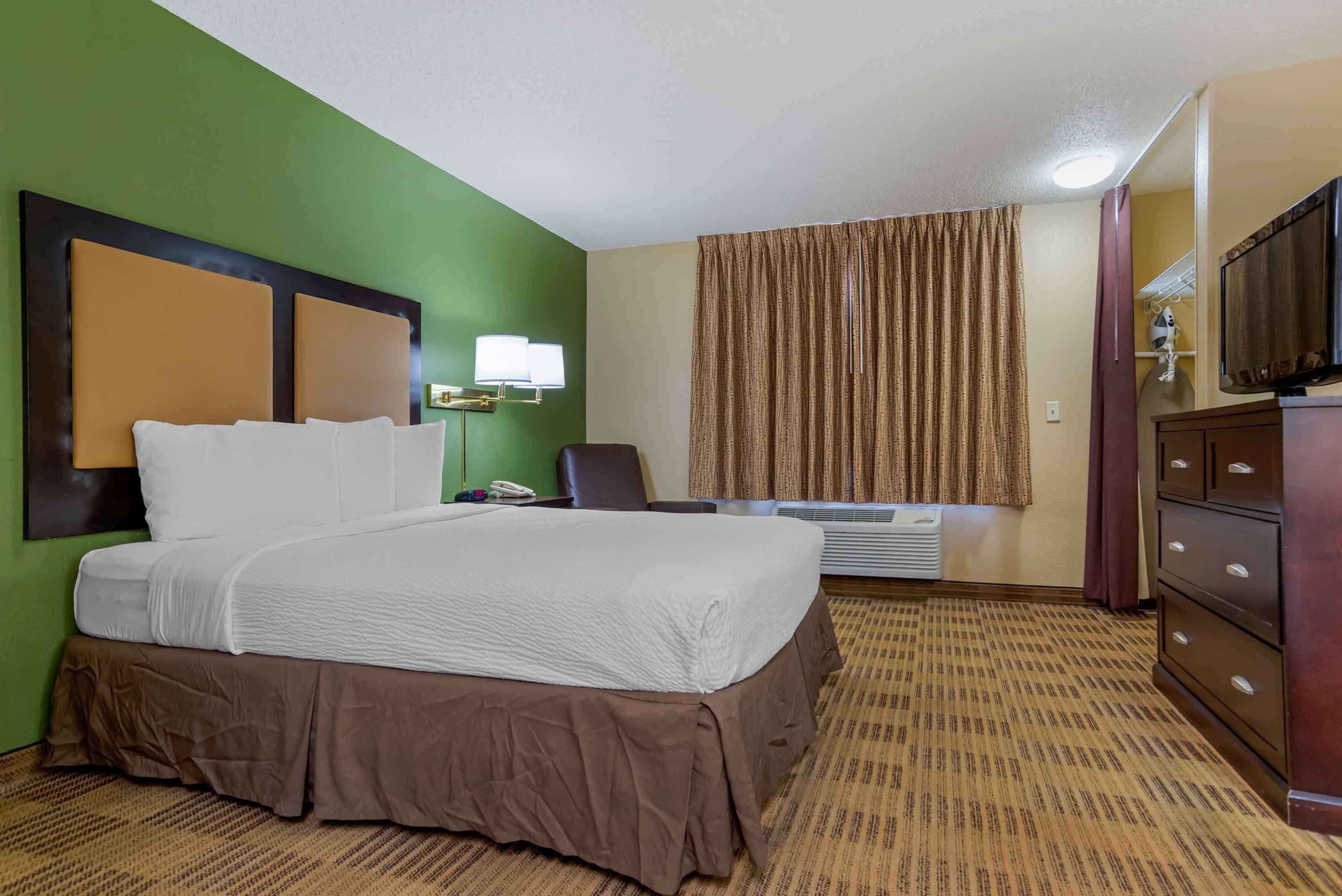 A hotel room with a large bed, a desk, a chair, a television, and a wardrobe.