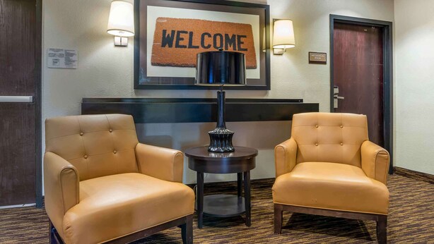 Un vestíbulo de hotel con dos sillones de cuero, un letrero de bienvenida, una lámpara y una mesa de recepción.