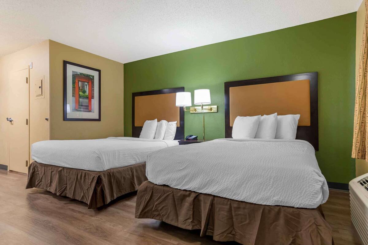 Ein Hotelzimmer mit zwei Betten, grünen Wänden und einem gerahmten Bild an der Wand.