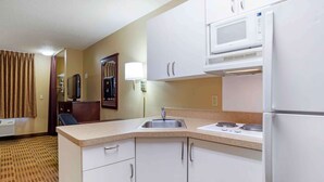 Cocina de hotel compacta con microondas, estufa, fregadero y armarios blancos.