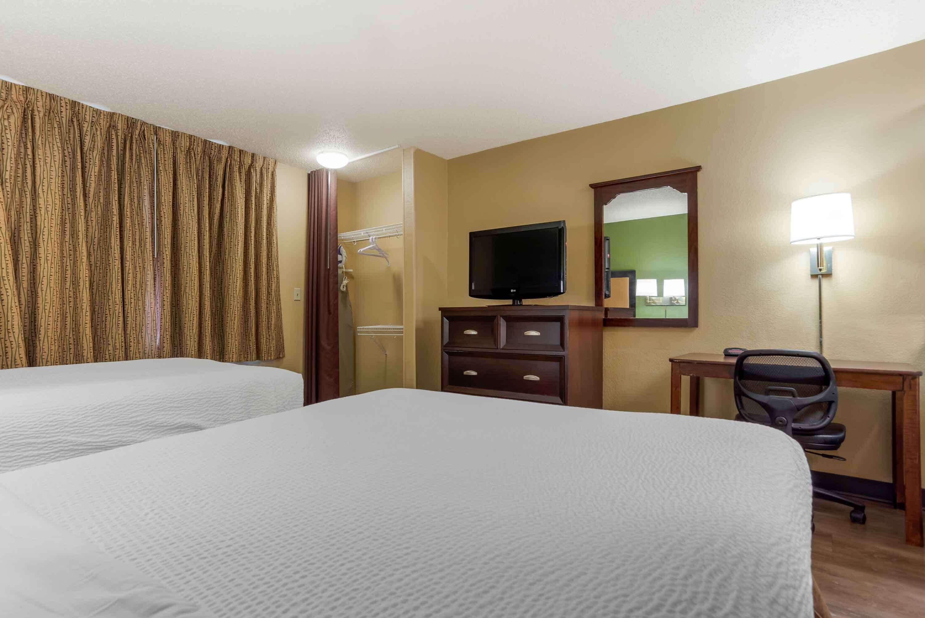 Habitación de hotel con dos camas, televisión, escritorio con silla, espejo y lámpara.