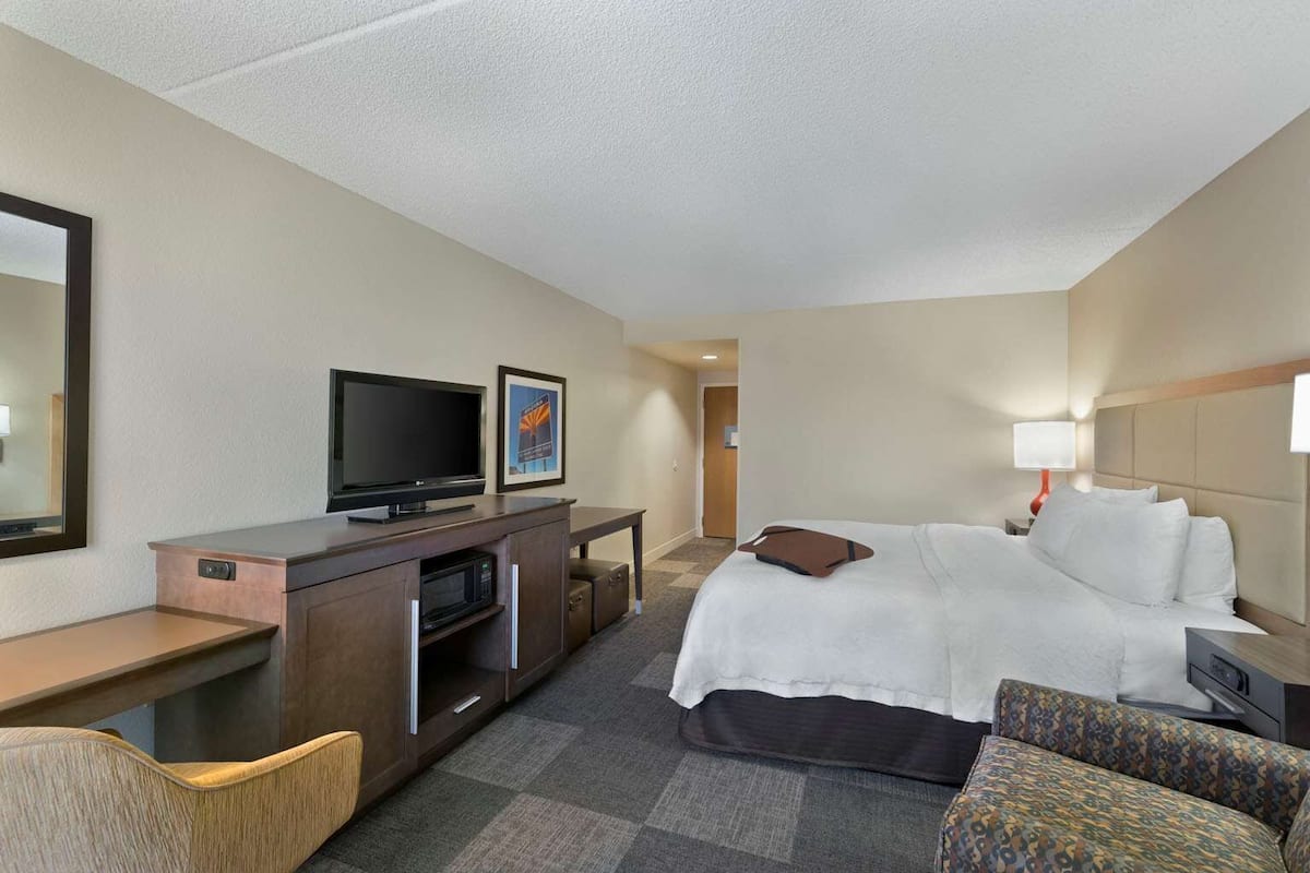 A hotel room with a bed, a desk with a television, a chair, and a small table.