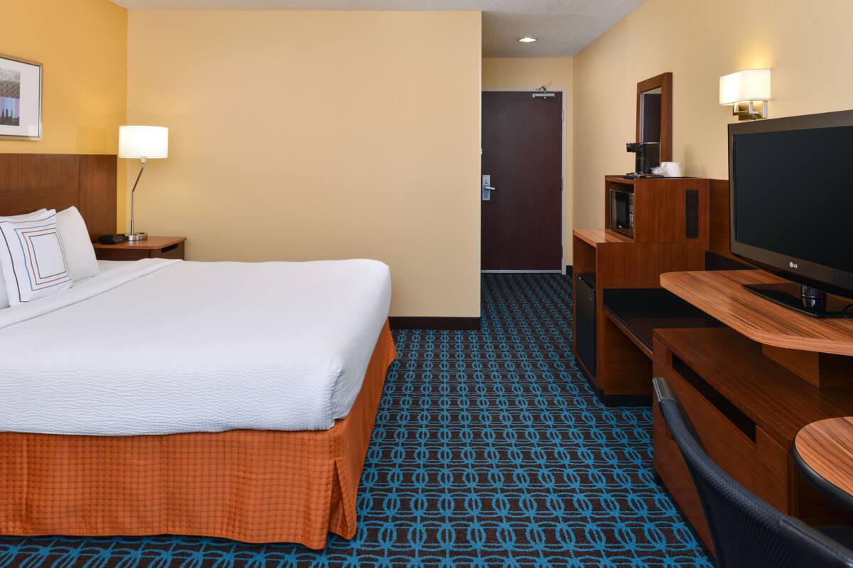 Une chambre d’hôtel avec un lit, un bureau, une télévision et une porte.