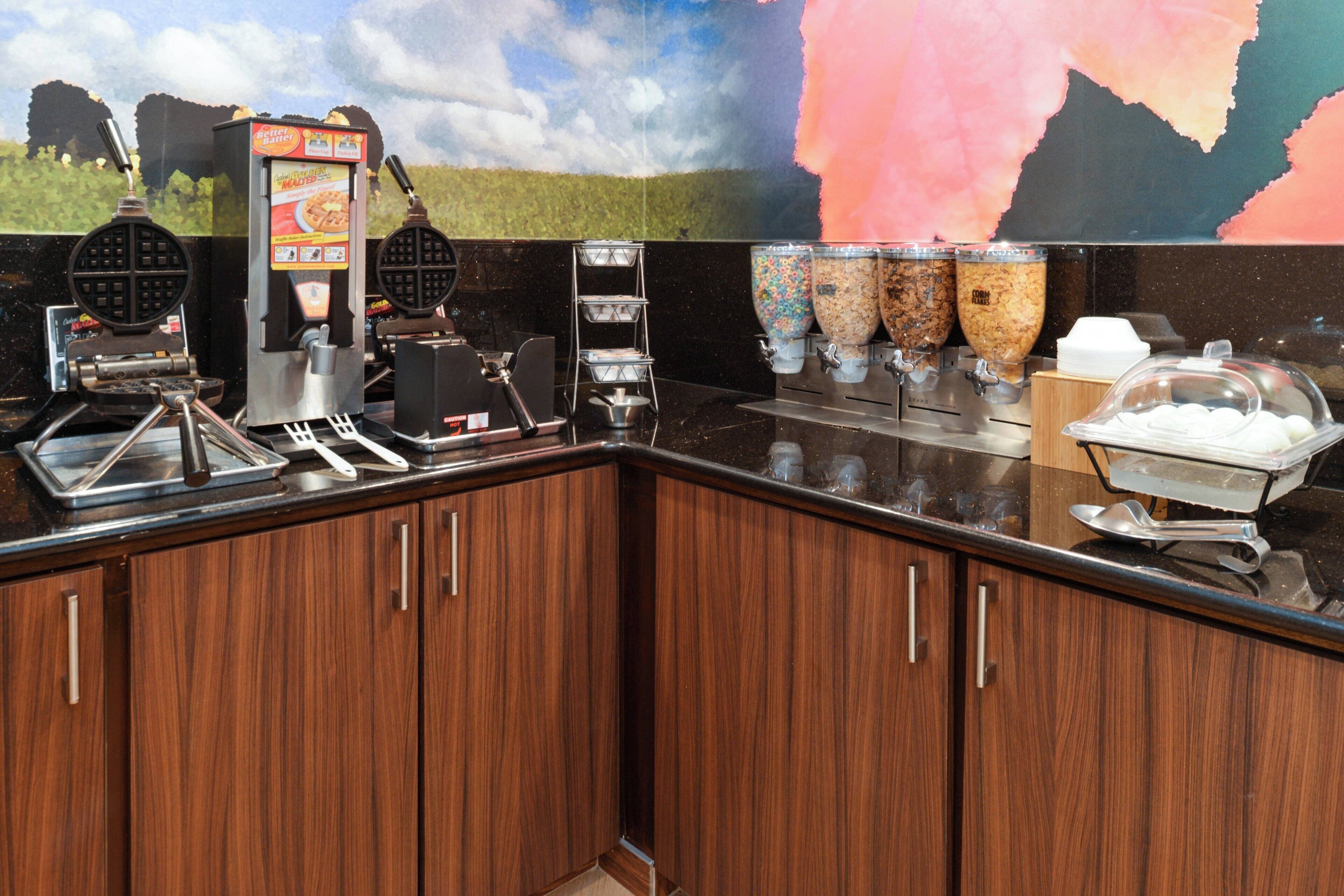 A kitchen area with waffle makers, a coffee machine, and food dispensers.