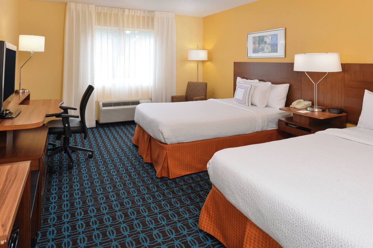 Une chambre d’hôtel avec deux lits, un bureau, une chaise, une lampe et un téléphone.