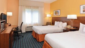 A hotel room with two beds, a desk with a computer, a chair, a TV, and a lamp.