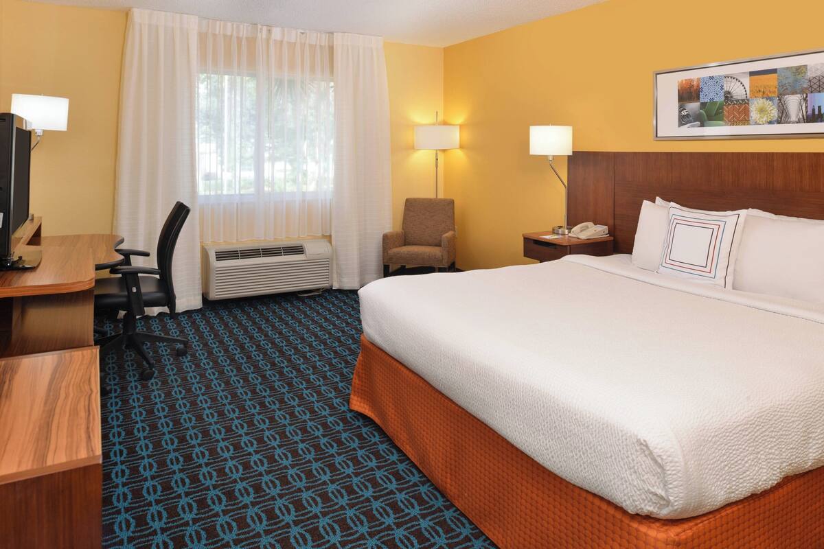 Une chambre d’hôtel avec un grand lit, un bureau avec un ordinateur, une chaise, une lampe et un tableau au mur.