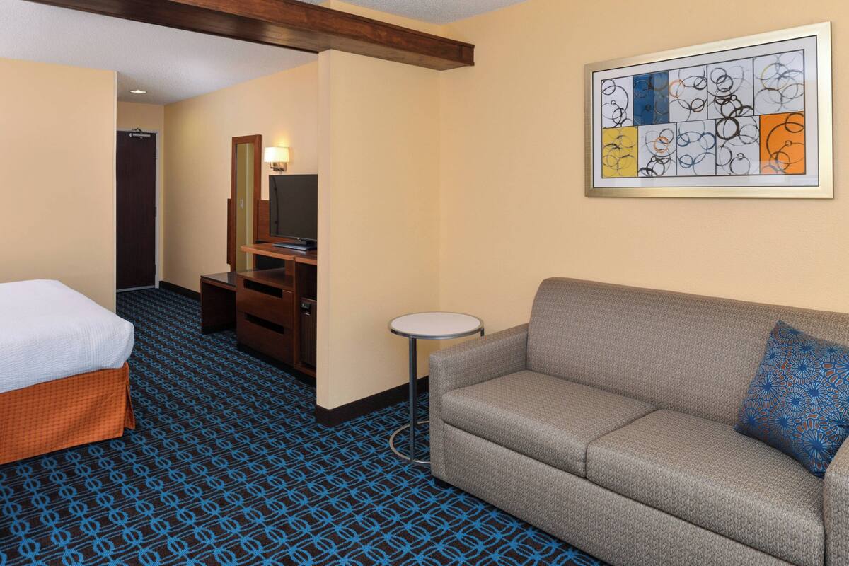 Une chambre d’hôtel avec un lit, un canapé, une petite table, un miroir et une œuvre d’art abstraite encadrée accrochée au mur.