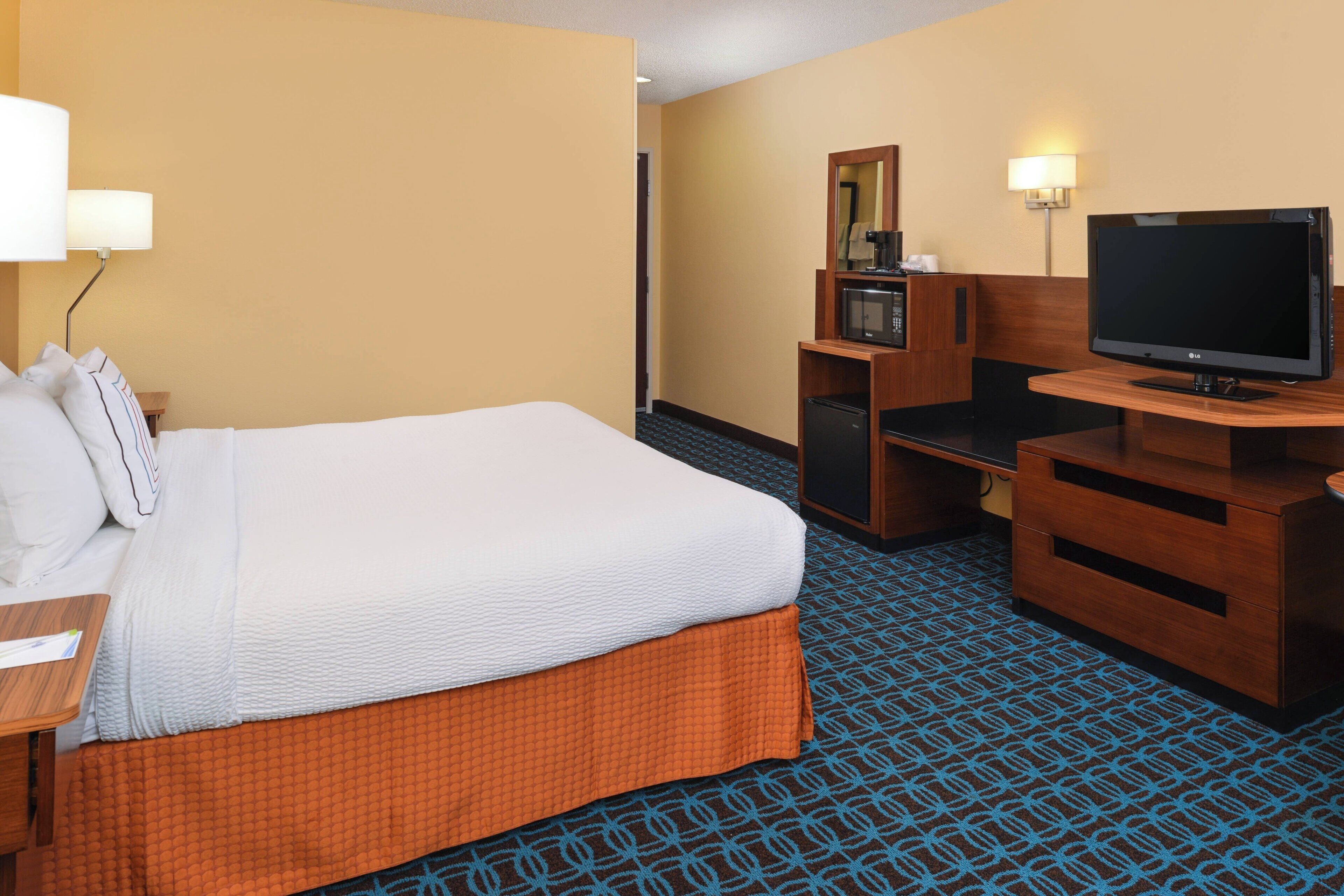 Una habitación de hotel con una cama, un escritorio, un televisor, un microondas y un aparador.