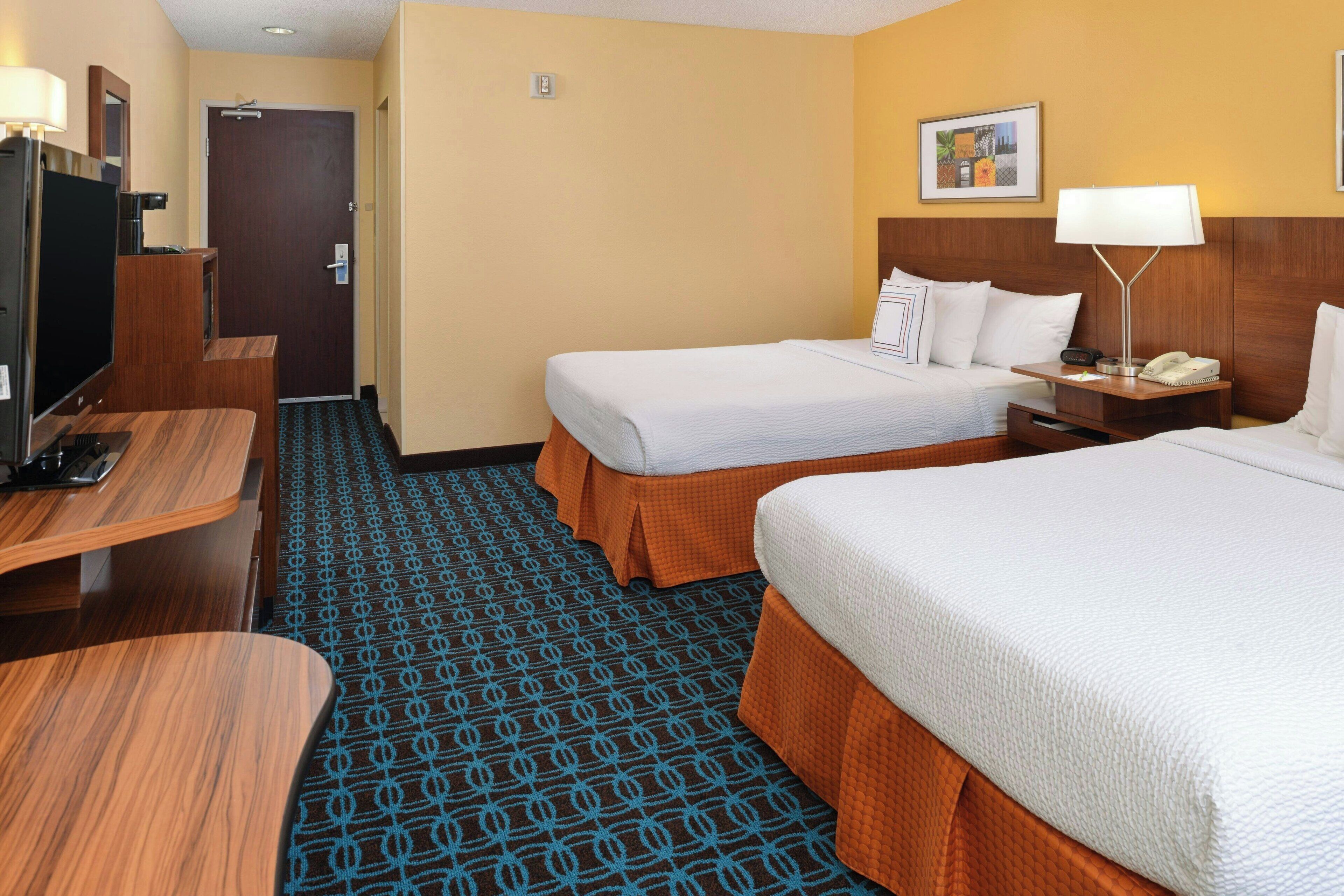 A hotel room with two beds, a desk, a TV, and a patterned carpet.