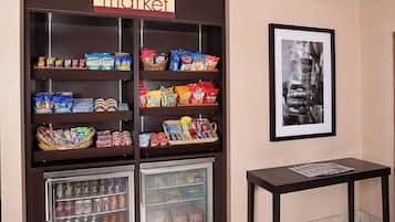 Exposição de petiscos e bebidas, com um letreiro 'market', uma foto emoldurada e uma pequena mesa com uma revista.
