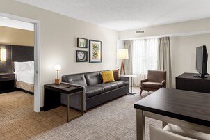 Habitación de hotel con cama, sofá, escritorio, silla, televisión y cuadros en la pared.