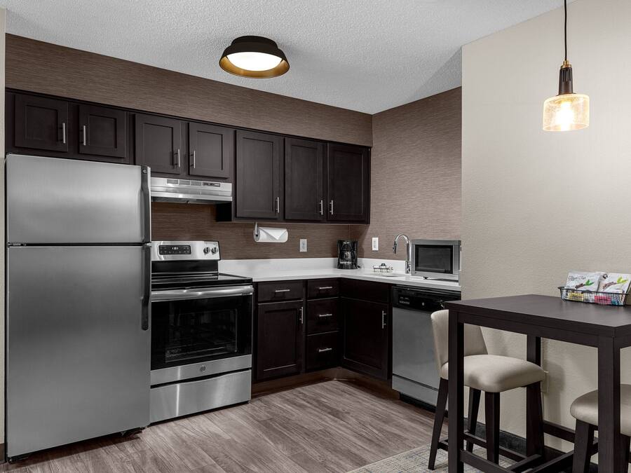 Una cocina moderna con armarios oscuros, electrodomésticos de acero inoxidable y una mesa de madera oscura con dos sillas.