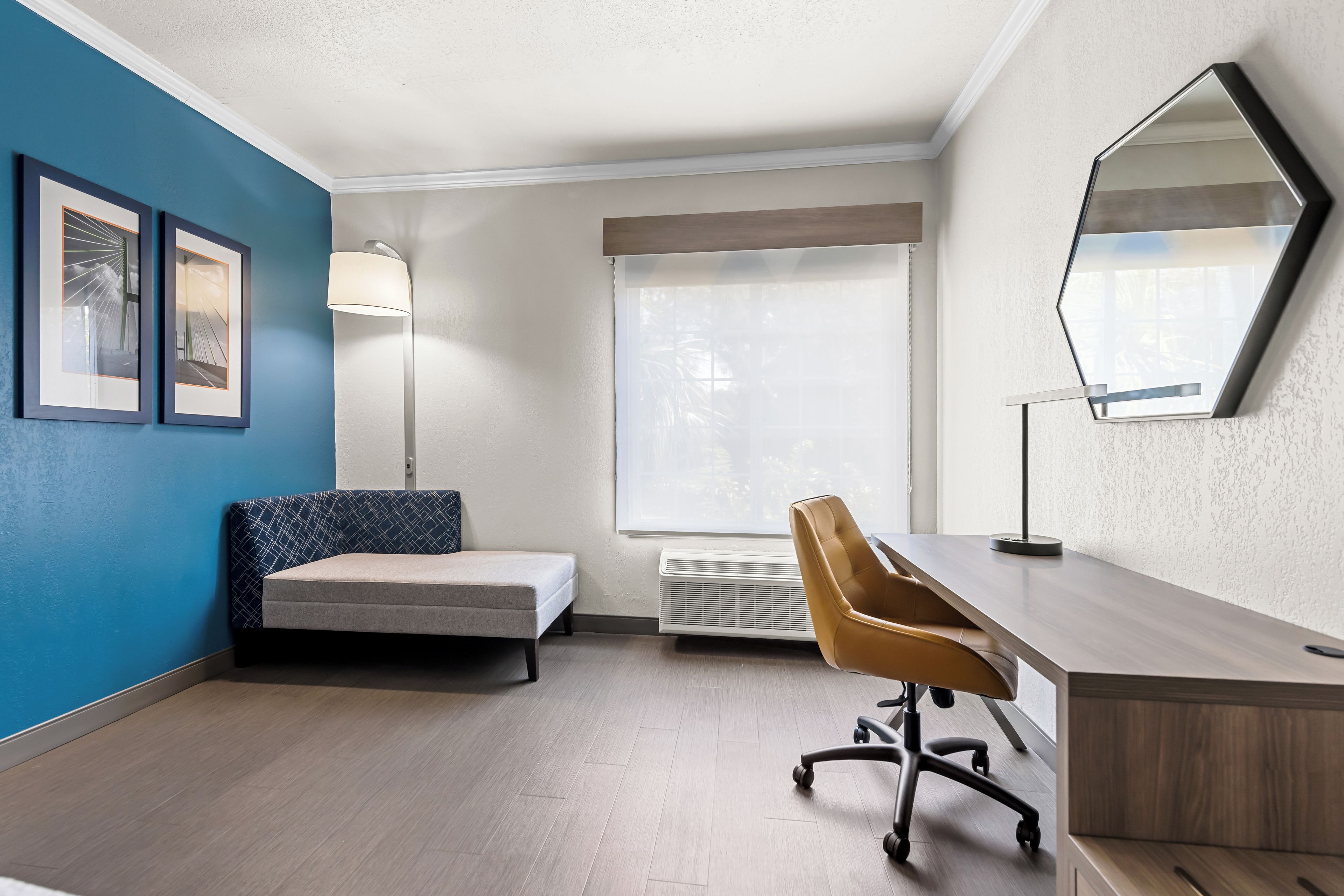 A modern room with a bed, desk, chair, and large window.