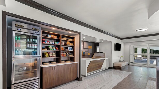 A modern kitchen area with a built-in refrigerator, pantry shelves stocked with snacks, and a seating area with a bench and a small table. - Holiday Inn Express Saint Simons Island by IHG (St. Simons Island)