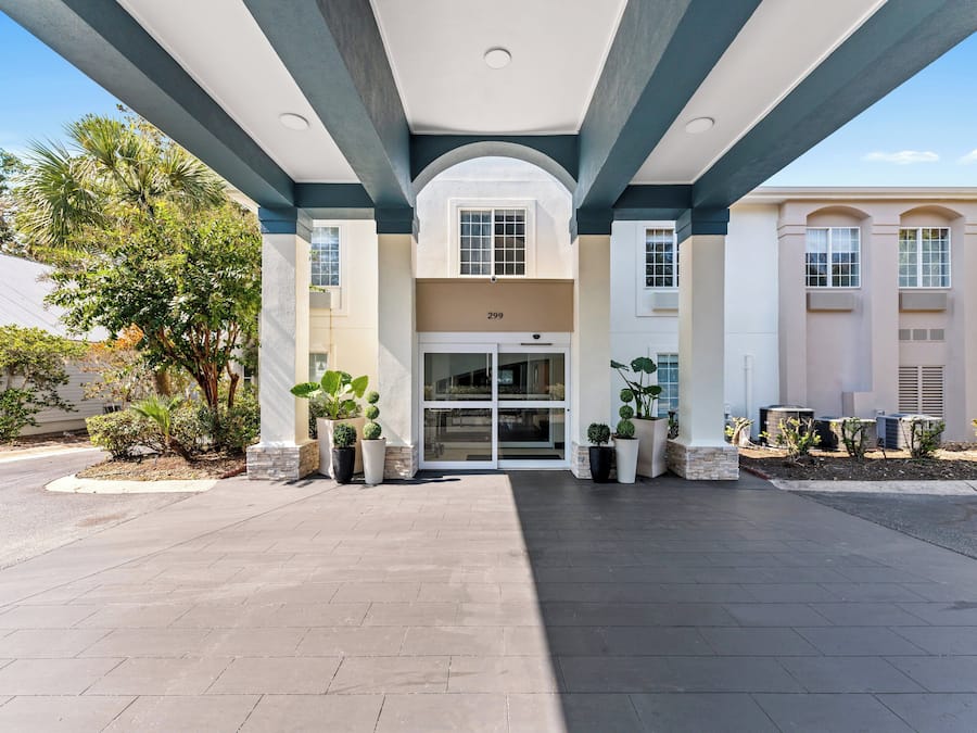A building entrance with a covered walkway, potted plants, and a clear sky.