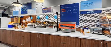 Un buffet pour le petit-déjeuner proposant une variété d’aliments, avec un panneau indiquant l’emplacement de la section boulangerie.