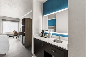 A hotel room with a bed, a desk, a chair, a minibar, a sink, and a large mirror. - Holiday Inn Express Saint Simons Island by IHG (St. Simons Island)
