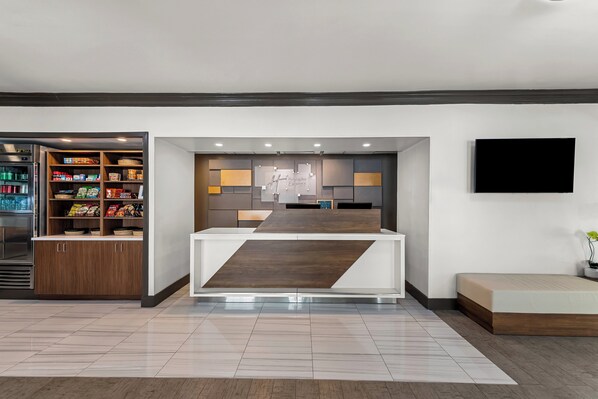 Un moderno vestíbulo de hotel con una zona de cocina, un televisor de pantalla plana y un espacio para sentarse.