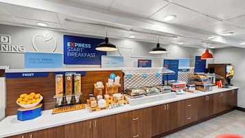 A breakfast bar with a variety of food options, including fruit, cereal, and bakery items.
