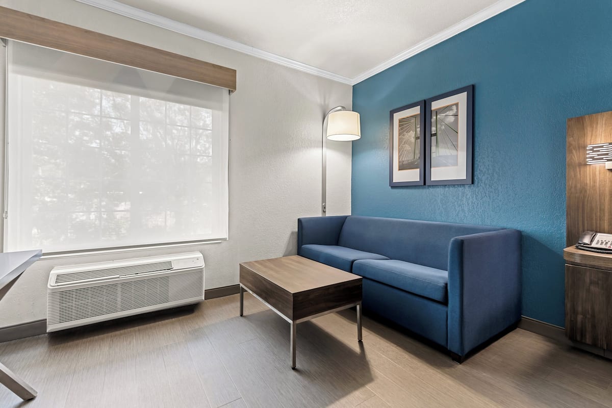A modern living room with a blue sofa, a wooden coffee table, a standing lamp, and a framed picture on the wall.