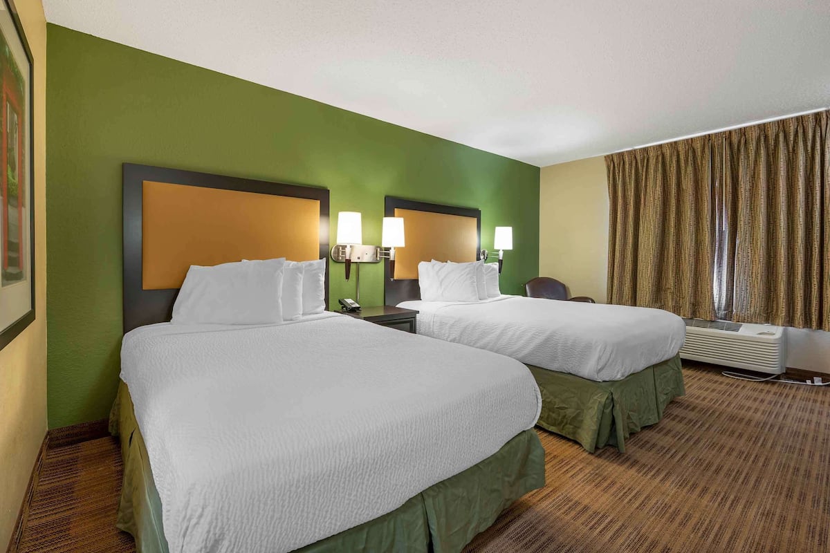 A hotel room with two beds, green walls, and a large window with curtains.