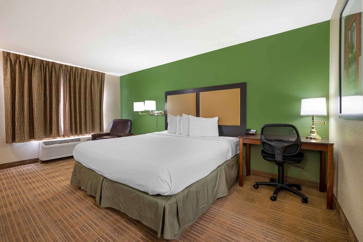 A hotel room with a large bed, a desk, a chair, and a window with curtains.
