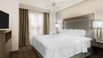 A hotel room with a bed, a desk, a chair, a television, a ceiling fan, and a window with curtains.