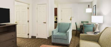 A hotel room with a television, a desk, a chair, a sofa, and a small table.