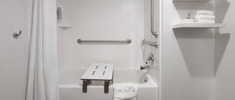 A bathroom with a white bathtub, a shower, a grab bar, a towel rack, and a shelf with folded towels.
