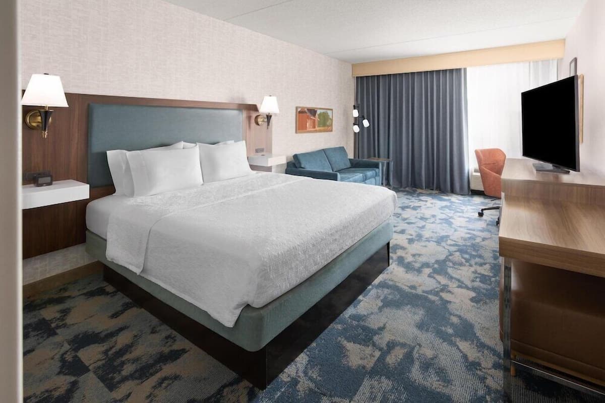 A hotel room with a large bed, a desk, a TV, and a seating area with a couch and chairs.