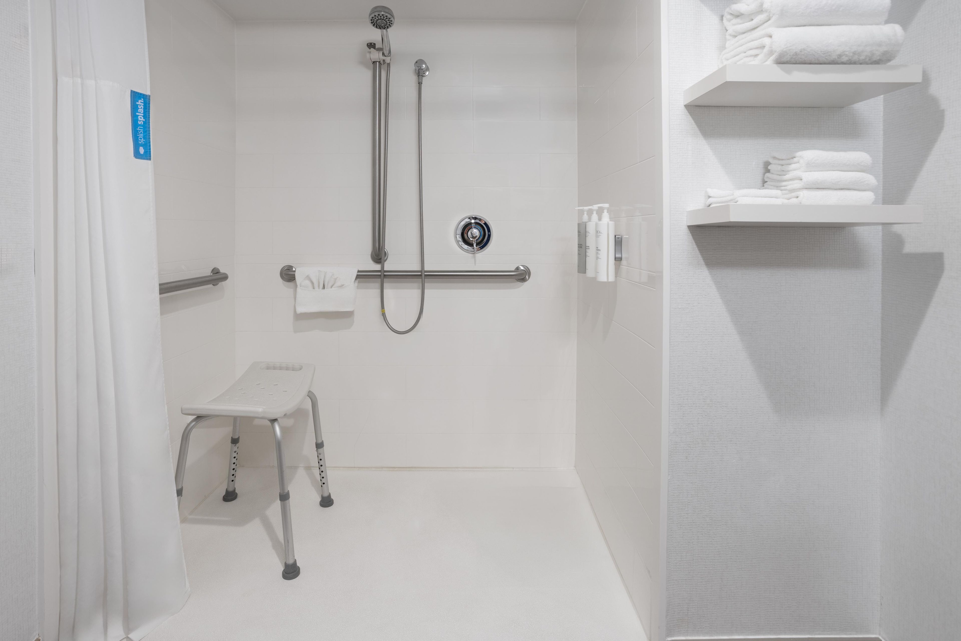 Un baño moderno con ducha, barra de apoyo, taburete y estante con toallas.