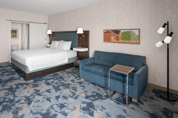 Une chambre d’hôtel avec un lit, un canapé, une table de chevet, une lampe et un tableau au mur.