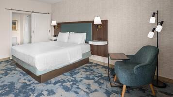 A hotel room with a large bed, a bedside table, a chair, and a floor lamp.