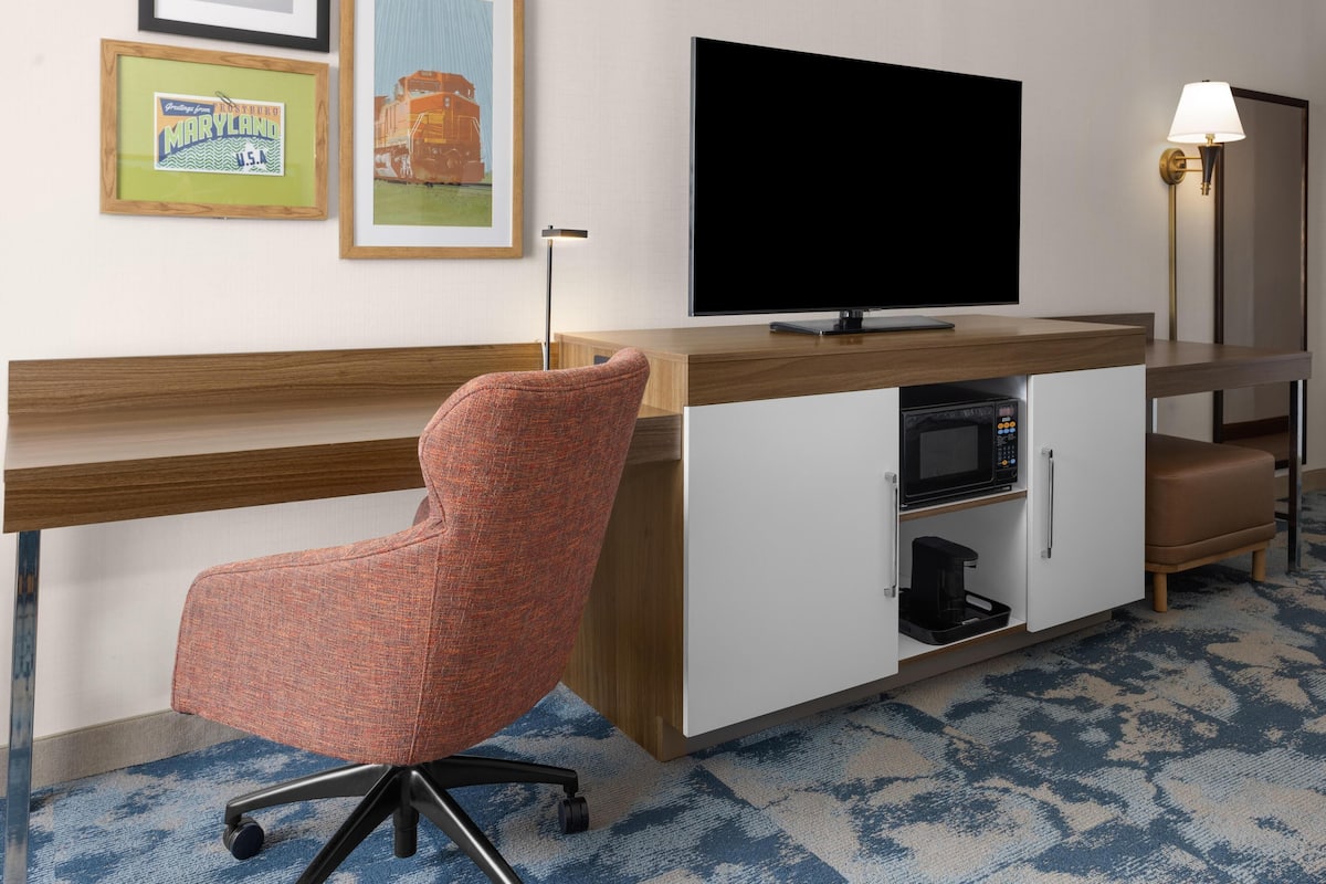 Une chambre d’hôtel équipée d’un bureau en bois, d’un téléviseur à écran plat, d’un four à micro-ondes et d’une machine à café.