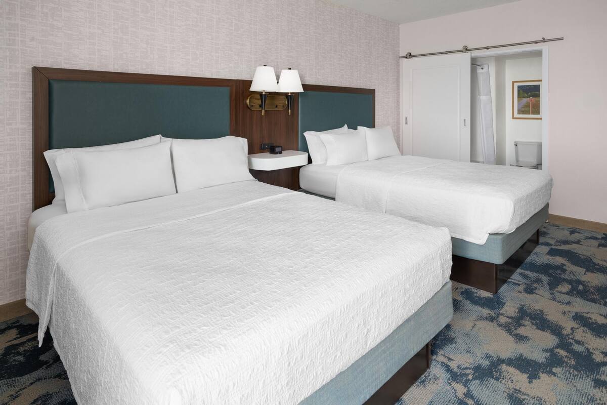 Une chambre d’hôtel avec deux lits, une table de chevet avec une lampe et une porte de salle de bain.
