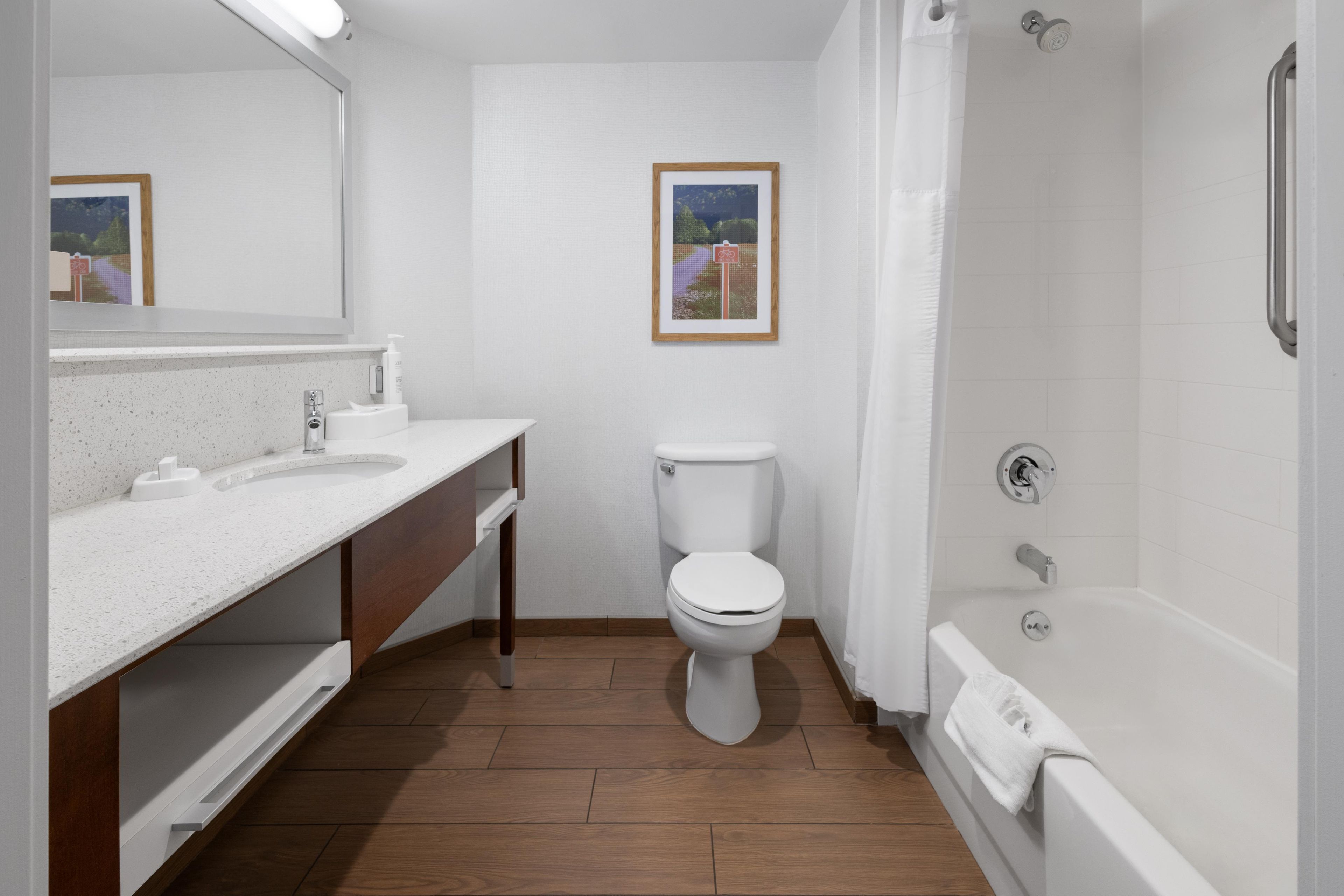 A bathroom with a white sink, toilet, and shower. There is a framed picture on the wall.